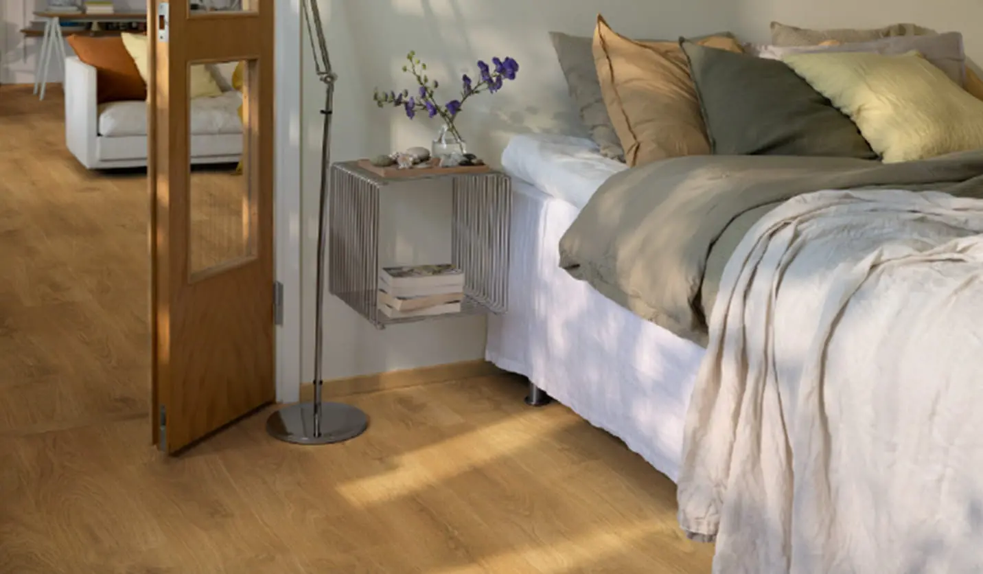 木製フローリングの上にあるベッドの横には、花瓶と本が置かれたモダンなサイドテーブルが設置されている