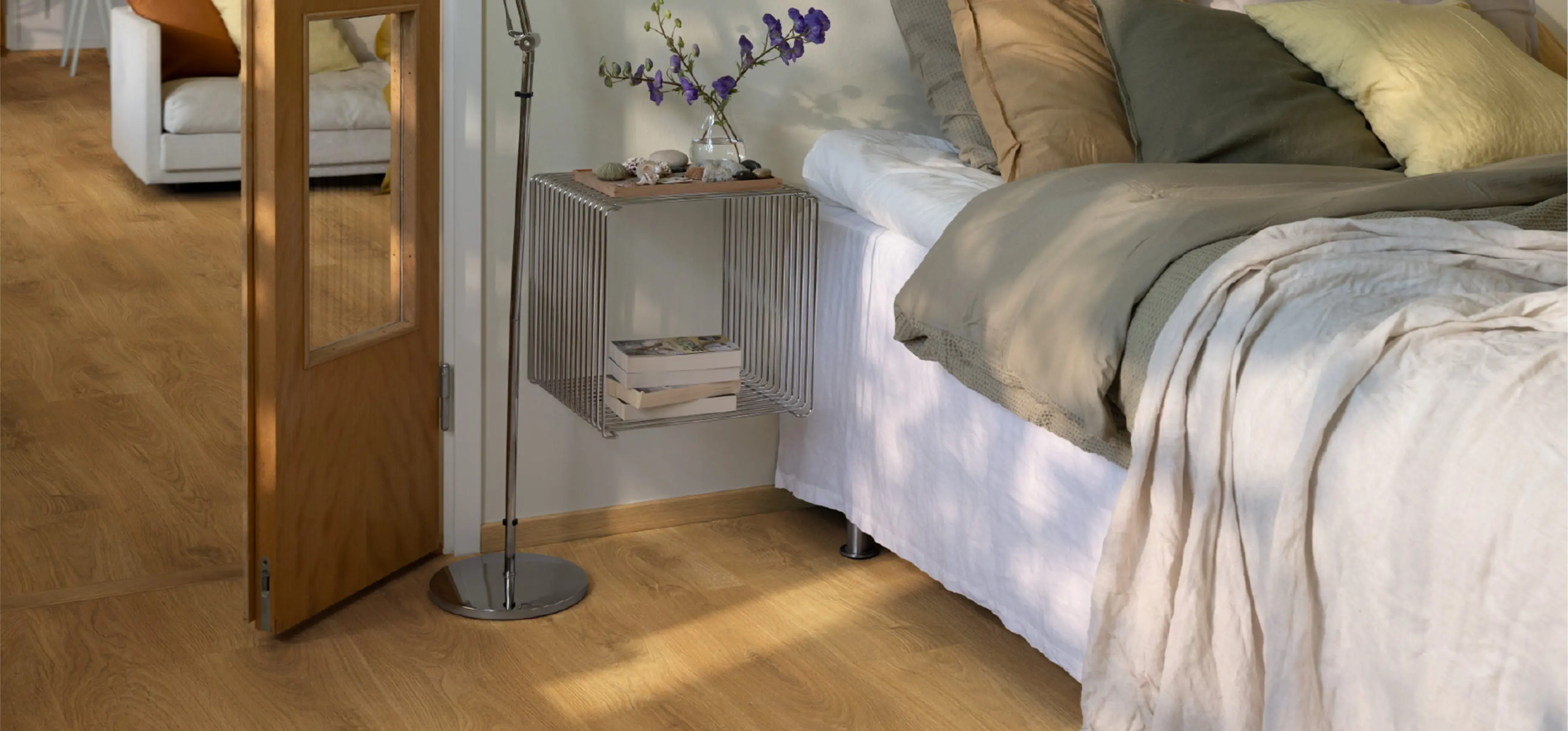 木製フローリングの上にあるベッドの横には、花瓶と本が置かれたモダンなサイドテーブルが設置されている